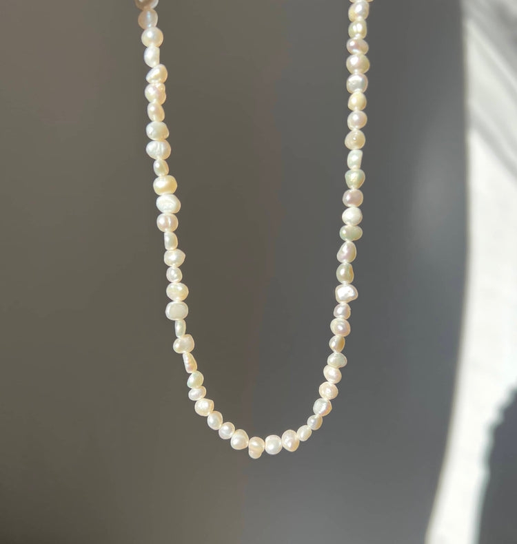 A beautiful pearl necklace featuring a silver chain adorned with lustrous white pearls, elegantly displayed against a soft grey background. This timeless piece radiates sophistication and charm, perfect for elevating any outfit or special occasion.